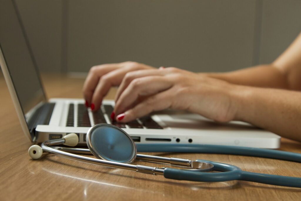 Laptop met een chatvenster naast een stethoscoop en een bril op een bureau