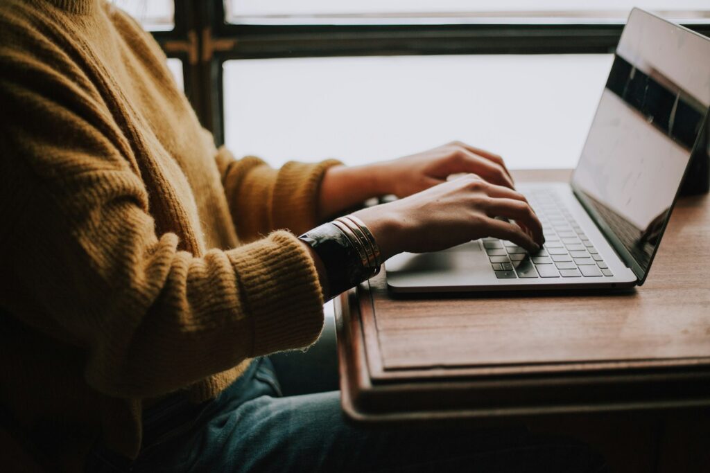 Student werkt op een laptop aan een scriptie in een bibliotheek met boeken en aantekeningen