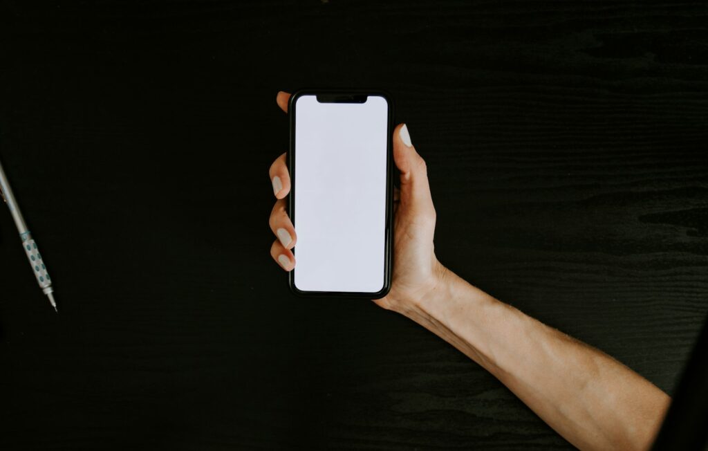 Iemand houdt een iPhone vast boven een bureau met een notitieboek